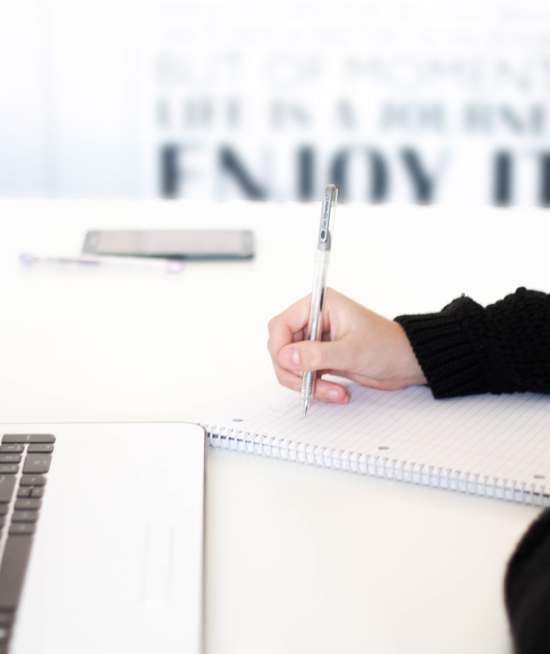 Femme qui prend des notes sur un carnet devant son ordinateur